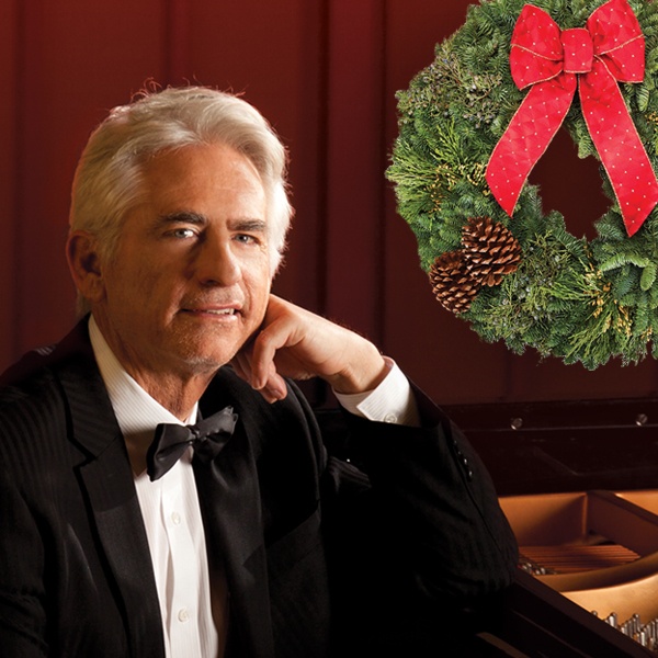 David Benoit at the piano with a Christmas wreath behind him.