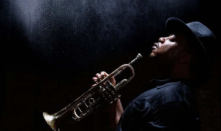 Nicholas Payton in profile, holding his trumpet.