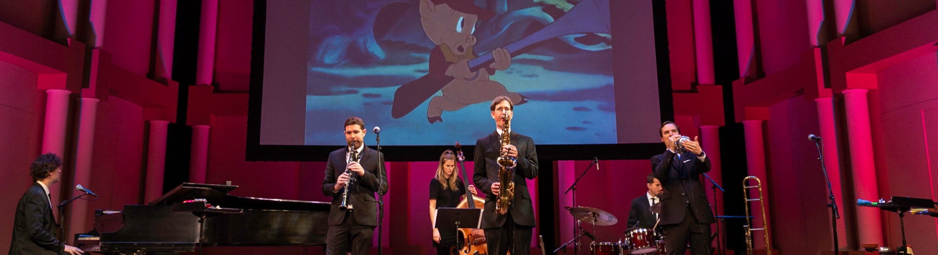 Members of the band performing on stage while a classic cartoon plays on a screen behind them.
