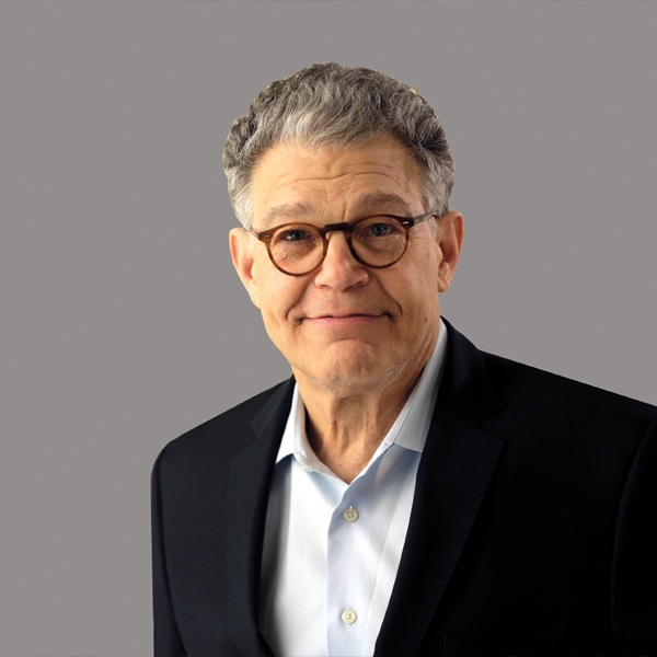 Al Franken in a dark blazer and white shirt, wearing glasses and looking at the camera against a gray background.