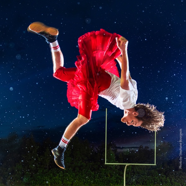 A member of the troupe caught in mid flip, a football goal in the distance.