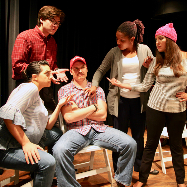 Five members of Capitol Comedy on stage gathered around a man in a red baseball cap.