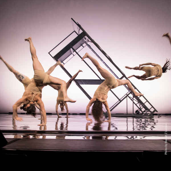 Several members of FLIP Fabrique upside down and pivoting across a stage with a platform in the background.