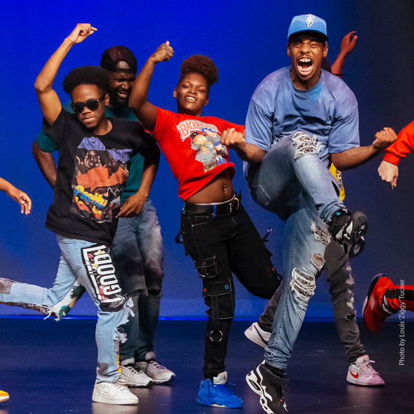 Several members of the dance troupe dancing on stage, exuberance displayed on their faces.