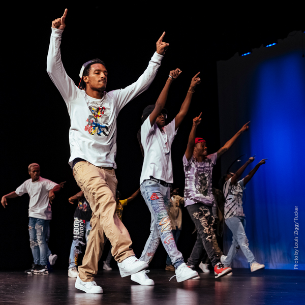 Four members of the dance troupe walking in sync with their arms raised up.