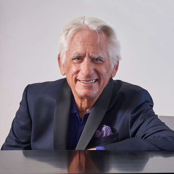 David Benoit in a dark jacket at the piano, smiling at the viewer.