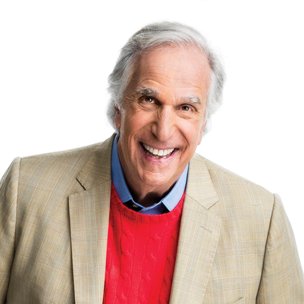 Henry Winkler in a red sweater and tan jacket smiling at the viewer.