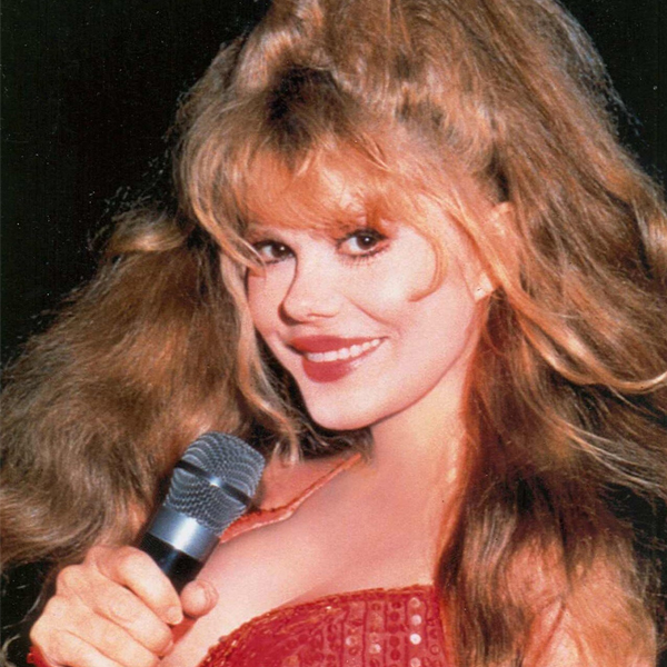 Charo in a red dress smiles at the camera and holds a microphone.
