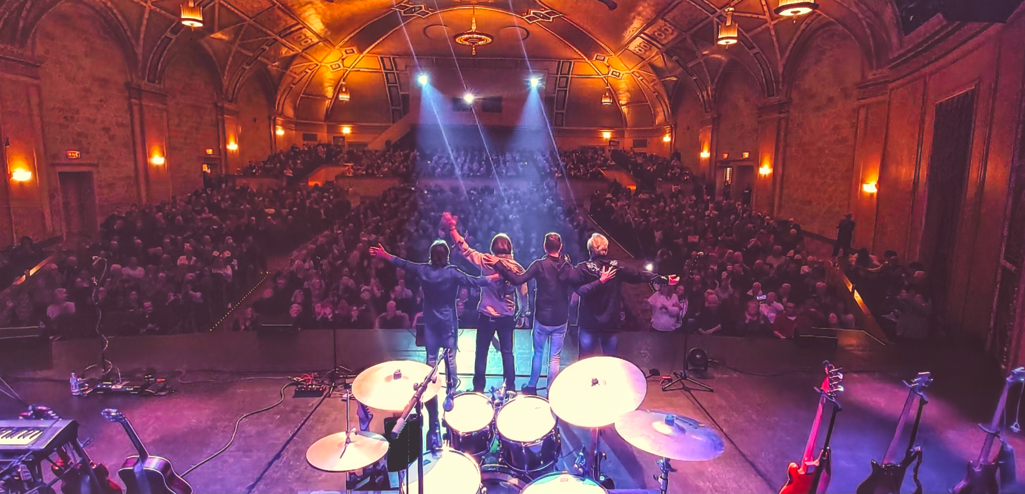 Members of Hotel California on a well-lit stage looking out at the audience in the background.