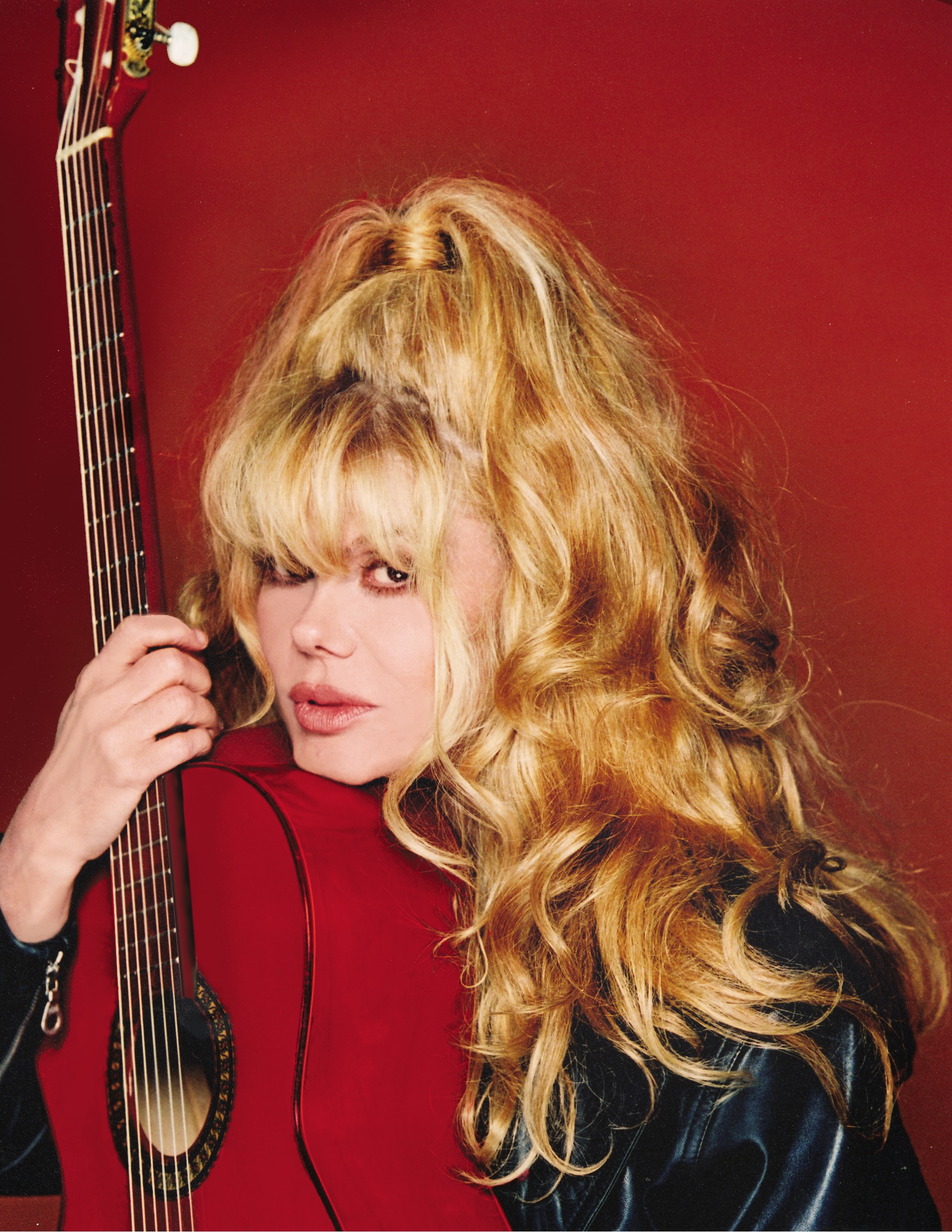 Charo holding the neck of an acoustic guitar against a deep red background