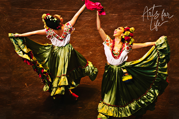 Two dancers from Pacífico Dance Company holding aloft their arms and the hem of their colorful costumes.