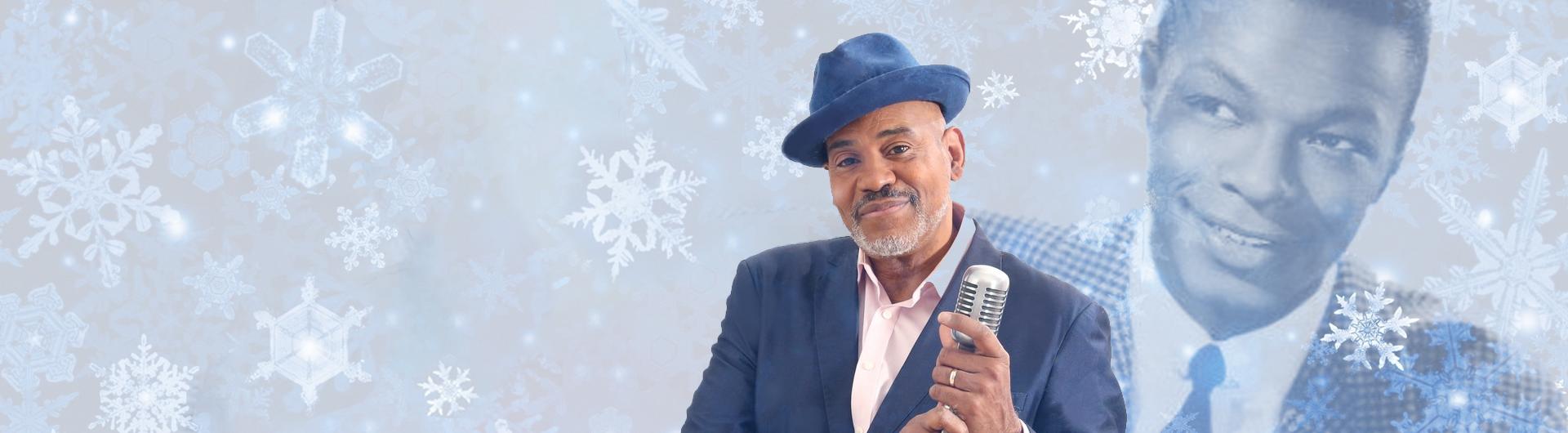 Allan Harris with Nat King Cole screened back in the background. Snowflakes are falling and Allan is in a blue suit, holding a microphone, a hat on his head.
