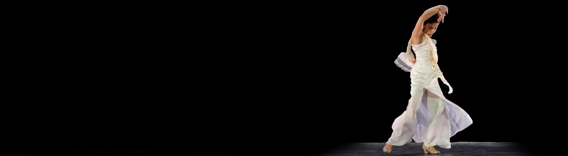 Soledad Barrio dancing with her arms raised against a dark background.