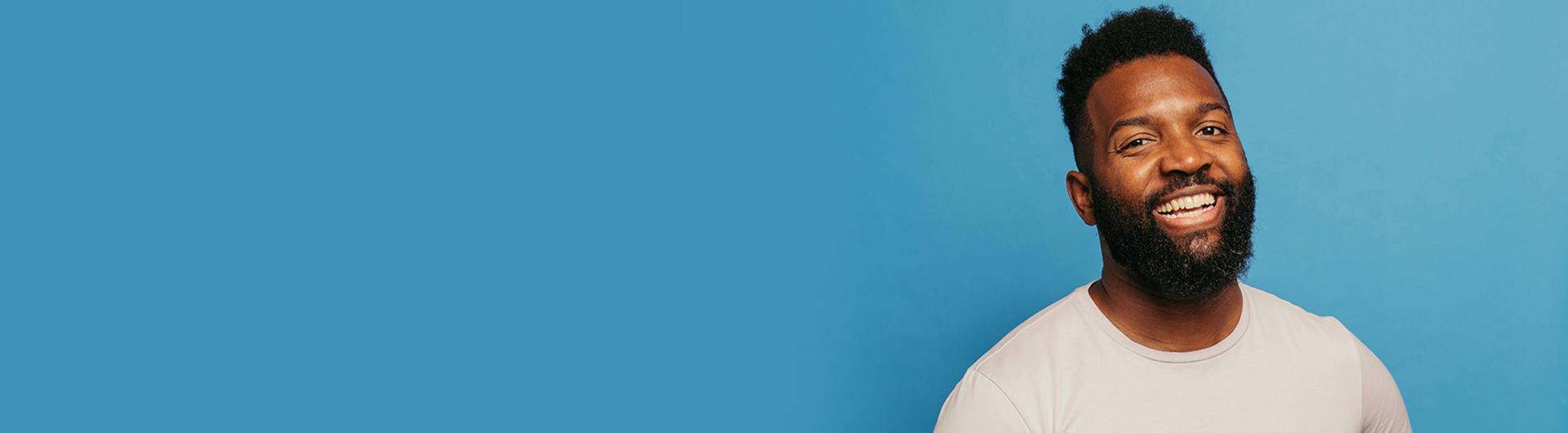 Baratunde Thurston smiling in a white shirt against a blue background.