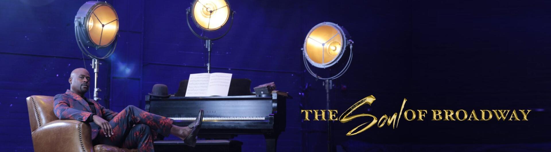Terron Brooks in a chair on stage, a piano and stage lights can be seen beside him.