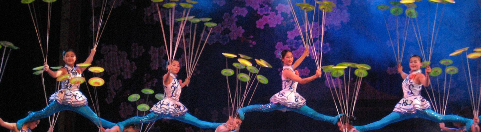 Members of The Peking Acrobats on stage plate spinning together in formation.