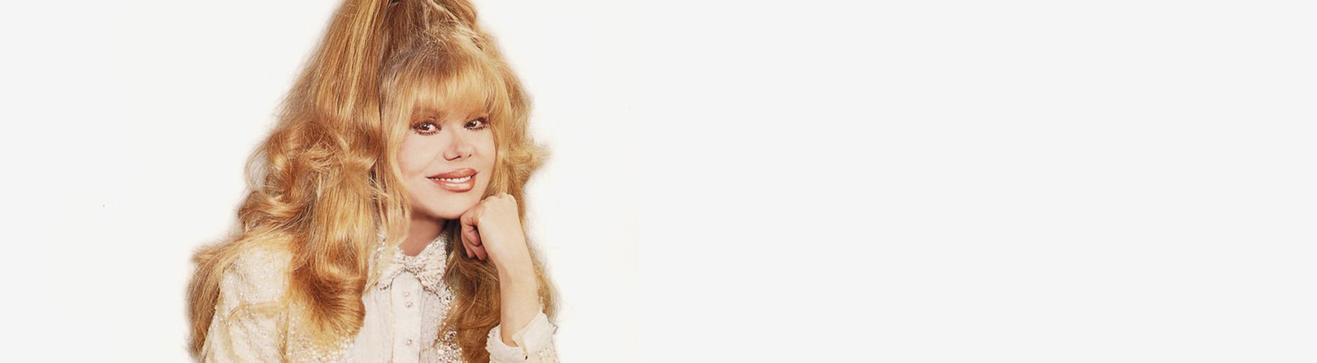 Charo in a light blouse smiles at the camera.