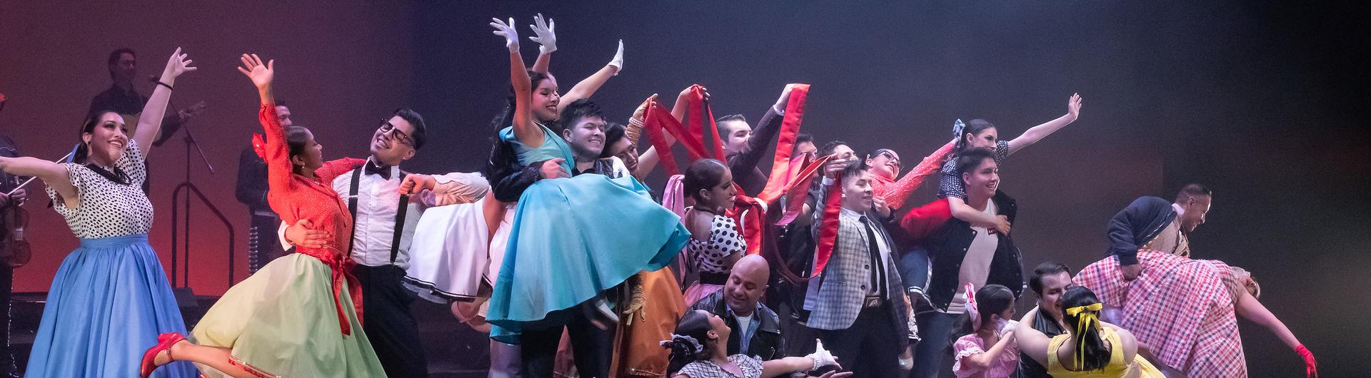 A large number of performers from Ballet Folklorico and Mariachi Garibaldi on stage, hands outstretched, the mood joyous and colorful.