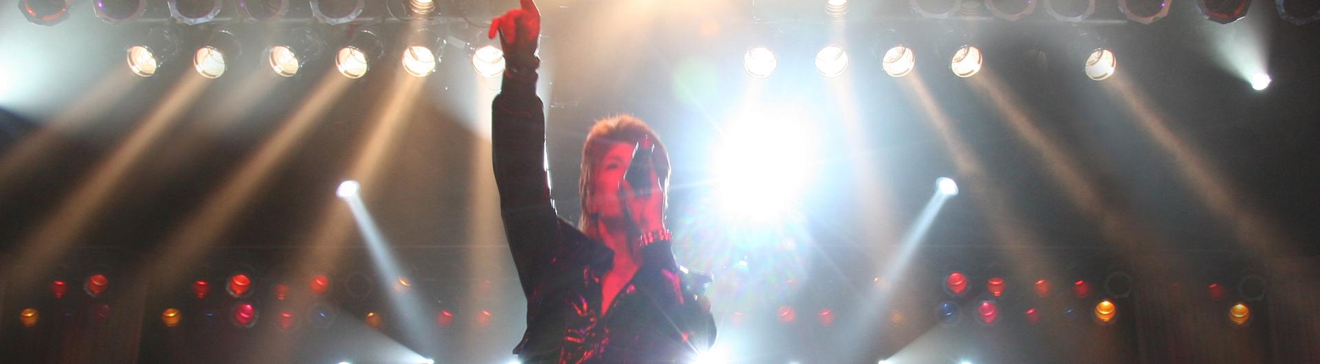 David Brighton as David Bowie on stage, a dozen stage lights shining on the stage behind him.