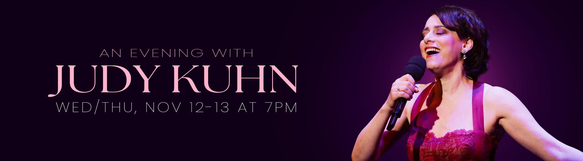 Judy Kuhn holding a microphone and singing against a dark background