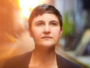 Anne Lanzilotti standing outdoors, blurred and stylized background.