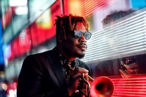 Keyon standing with his trumpet beside a wall of colored glass.