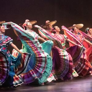 Dancers from Ballet Folklorico in colorful dresses on stage. Musicians from Mariachi Garibaldi stand in the background.