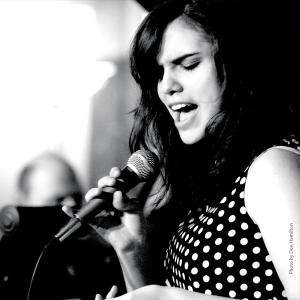 Julie Keefe in a white-dotted top holding a microphone and singing