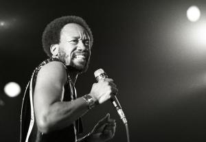 A black and white photo of Maurice White on stage holding a microphone
