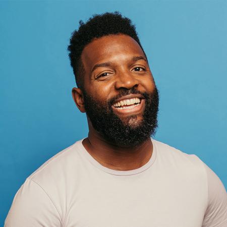 Baratunde Thurston smiling in a pale top against a light blue-green background