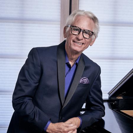 David Benoit in glasses and a suit leaning against a grand piano