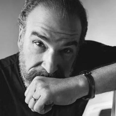 Mandy Patinkin looking deeply into the camera, one hand pressed against his chin