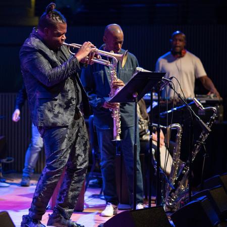 Members of Miles Electric Band on stage performing on trumpet and saxophone