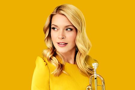 Bria Skonberg in a yellow top holding a trumpet against a yellow background.