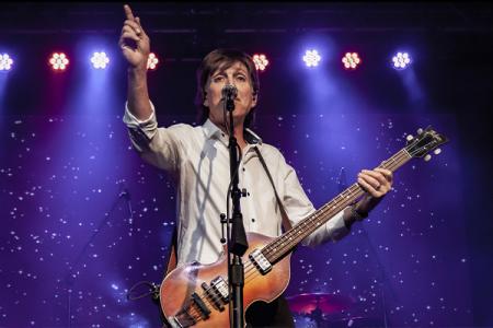 Tony Kishman holding a guitar and pointing, as Paul McCartney.