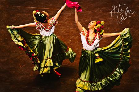 Two dancers from Pacífico Dance Company holding aloft their arms and the hem of their colorful costumes.