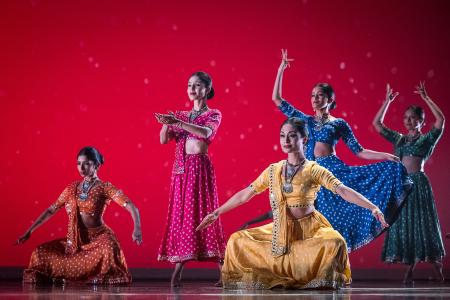 Sa Dance Company performers in colorful traditional dress dance against a vivid red backdrop.
