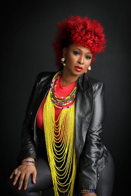 Portrait of Mumu Fresh wearing a black leather jacket, red top, and layered colorful beaded necklaces.
