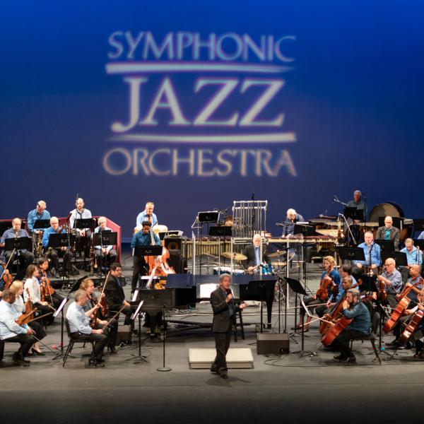 Symphonic Jazz Orchestra on stage, their logo projected behind them on a blue background.