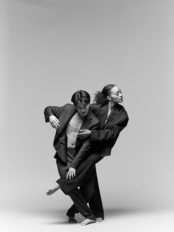 Two dancers in dark jackets intertwined against a gray background.