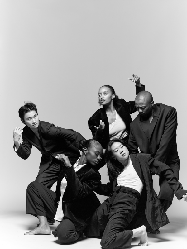 Five members of A.I.M in dark jackets posed in a group, each looking in a different direction, against a gray background